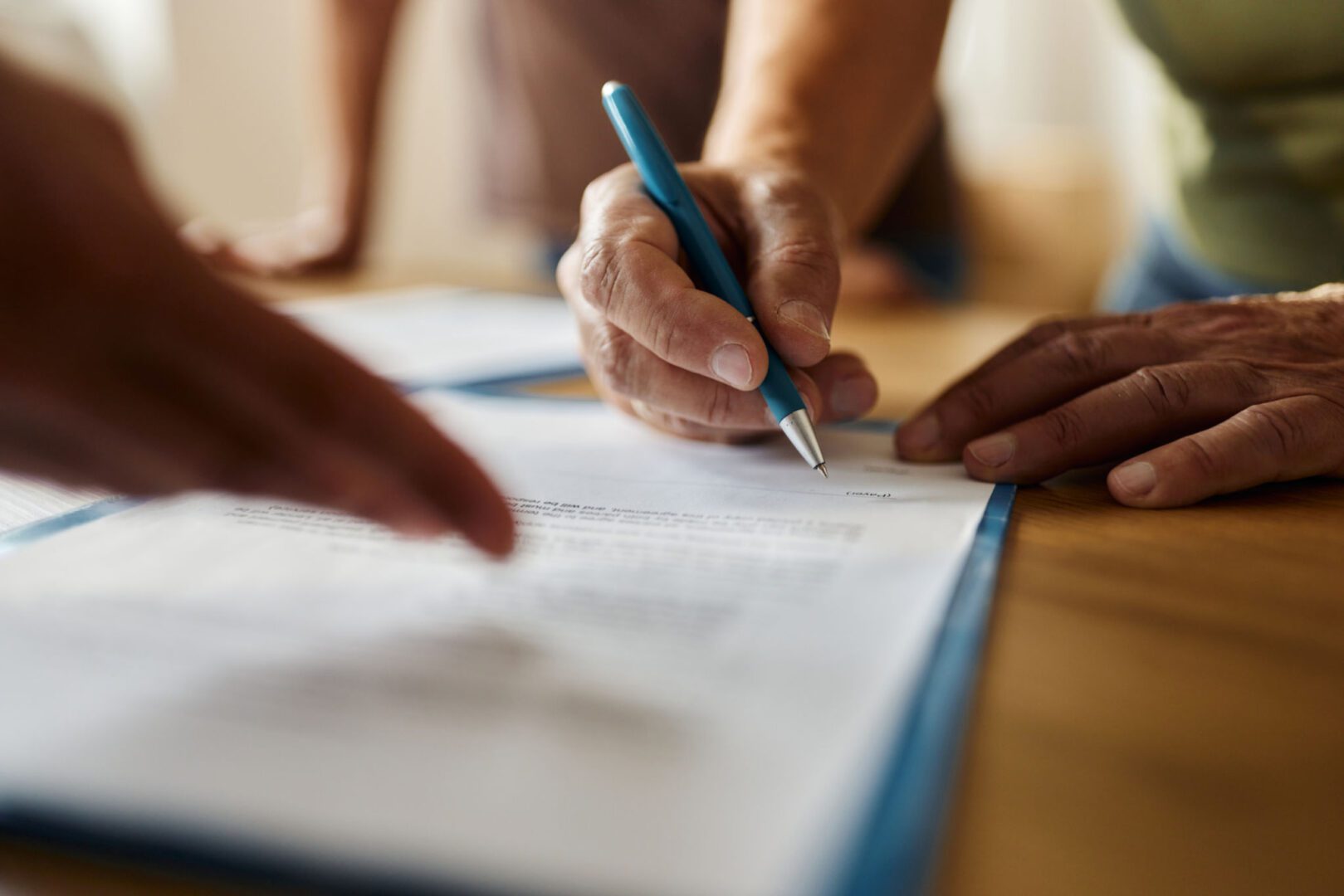 Hands signing a document with blue pen.