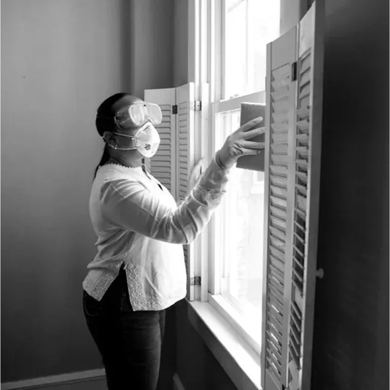 Person wearing headphones and adjusting window blinds indoors.