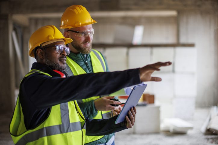 Two construction workers in helmets discussing plans on site.
