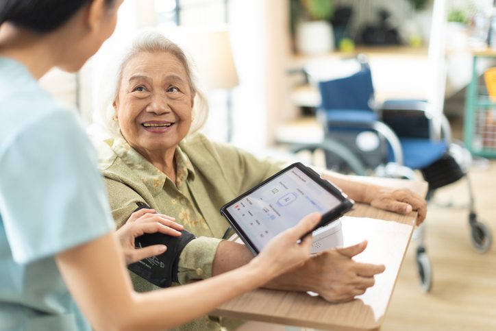 Elderly woman happily using a tablet with assistance.