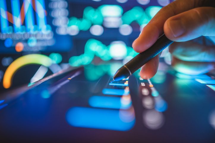 A hand using a stylus on a digital touchscreen with financial data.